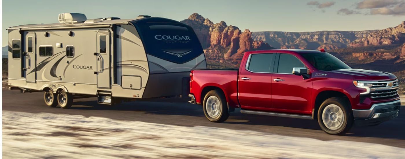 A red 2026 Chevy Silverado 1500 LTZ is towing a camper.