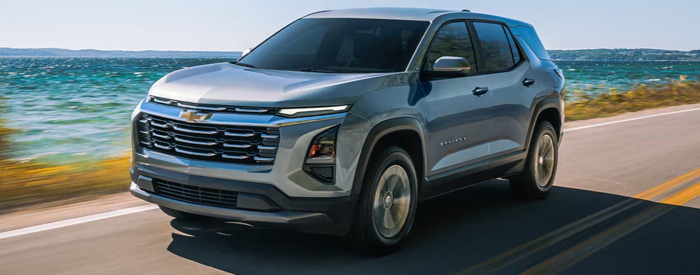 Grey 2026 Chevy Equinox driving along the water on a paved road.