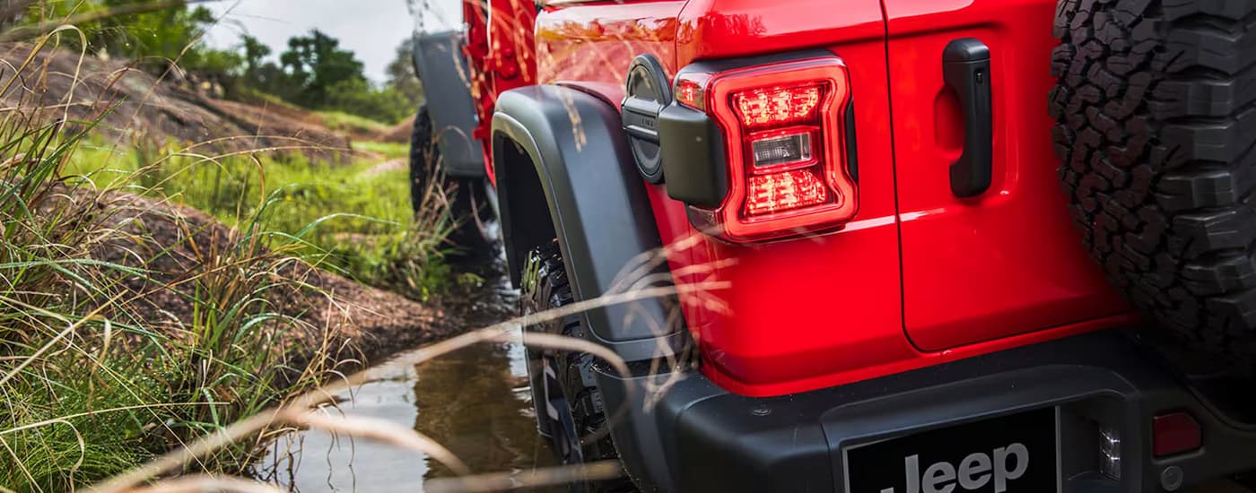 Red 2026 Jeep Wrangler off-roading through a muddy river