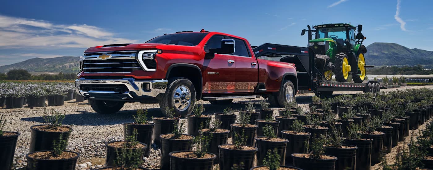 Red 2025 Chevy Silverado 3500 HD towing a green tractor on a trailer.