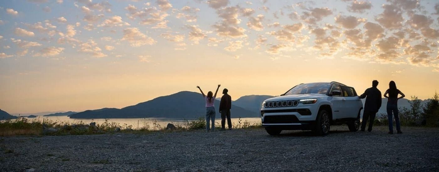 White 2025 Jeep Compass parked near a lake at dusk
