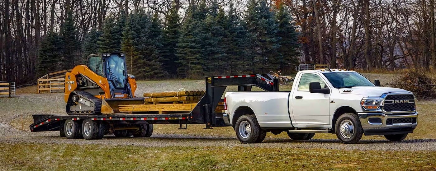 A white 2024 Ram 3500 towing a skid-steer.